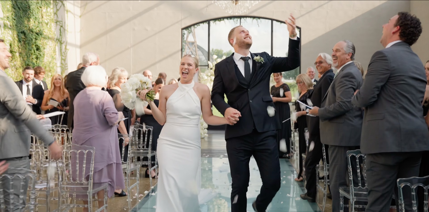 Bride and groom walking back down the aisle through falling petals, guests on their feet