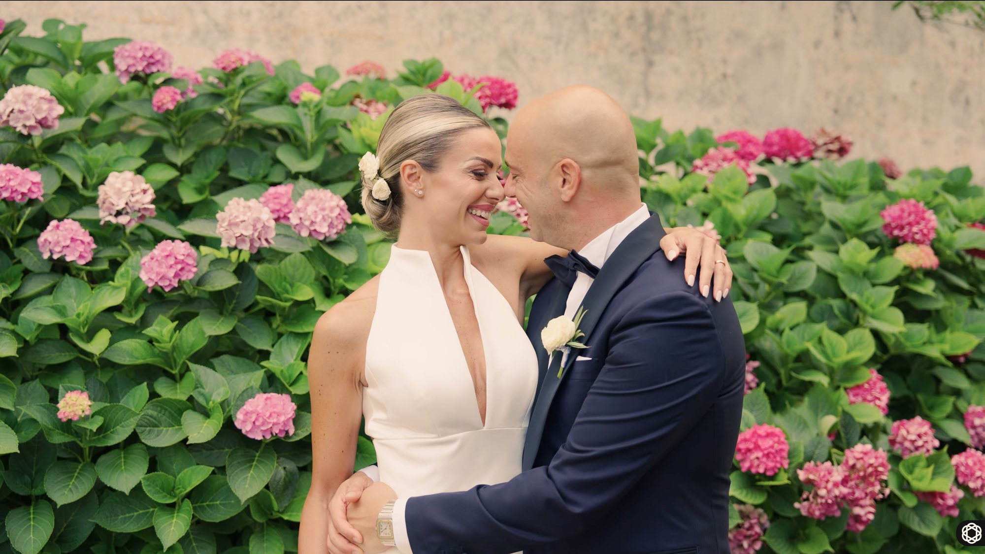 Bride and groom laughing together in front of a wall of pink and white hydrangeas