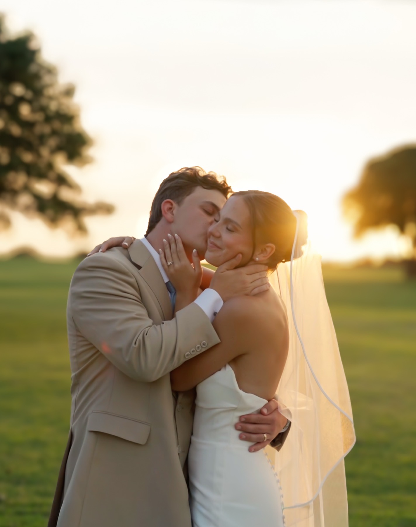 Bride and groom kissing at golden hour, her veil lit from behind by the low sun