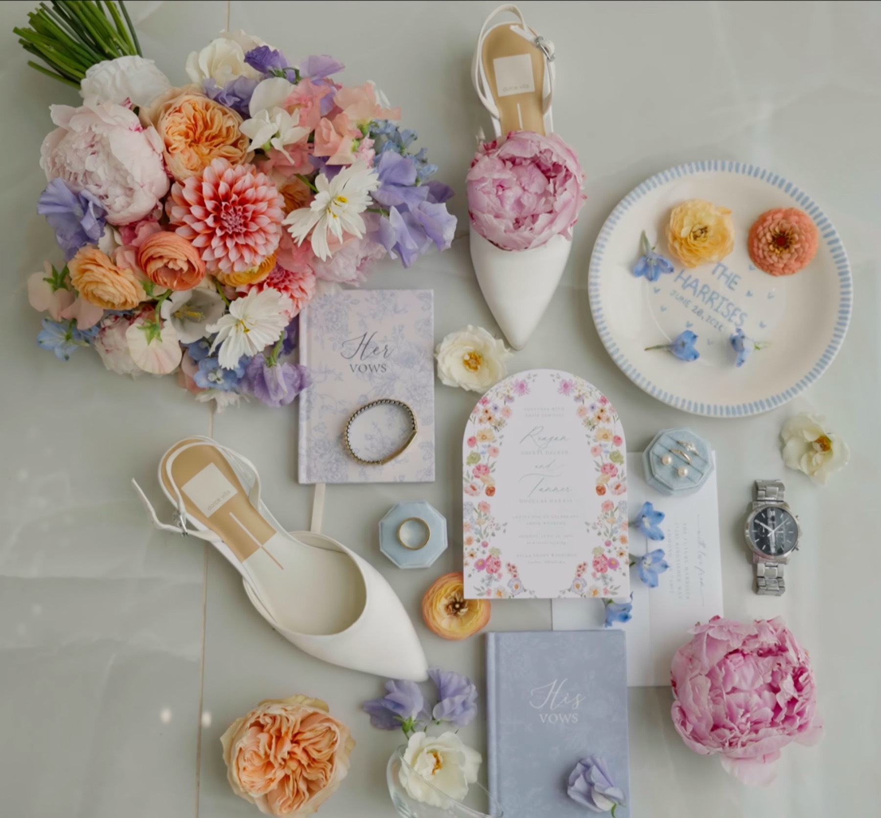 Flat-lay of the day's details — bouquet, shoes, vow books, invitation, rings and a watch