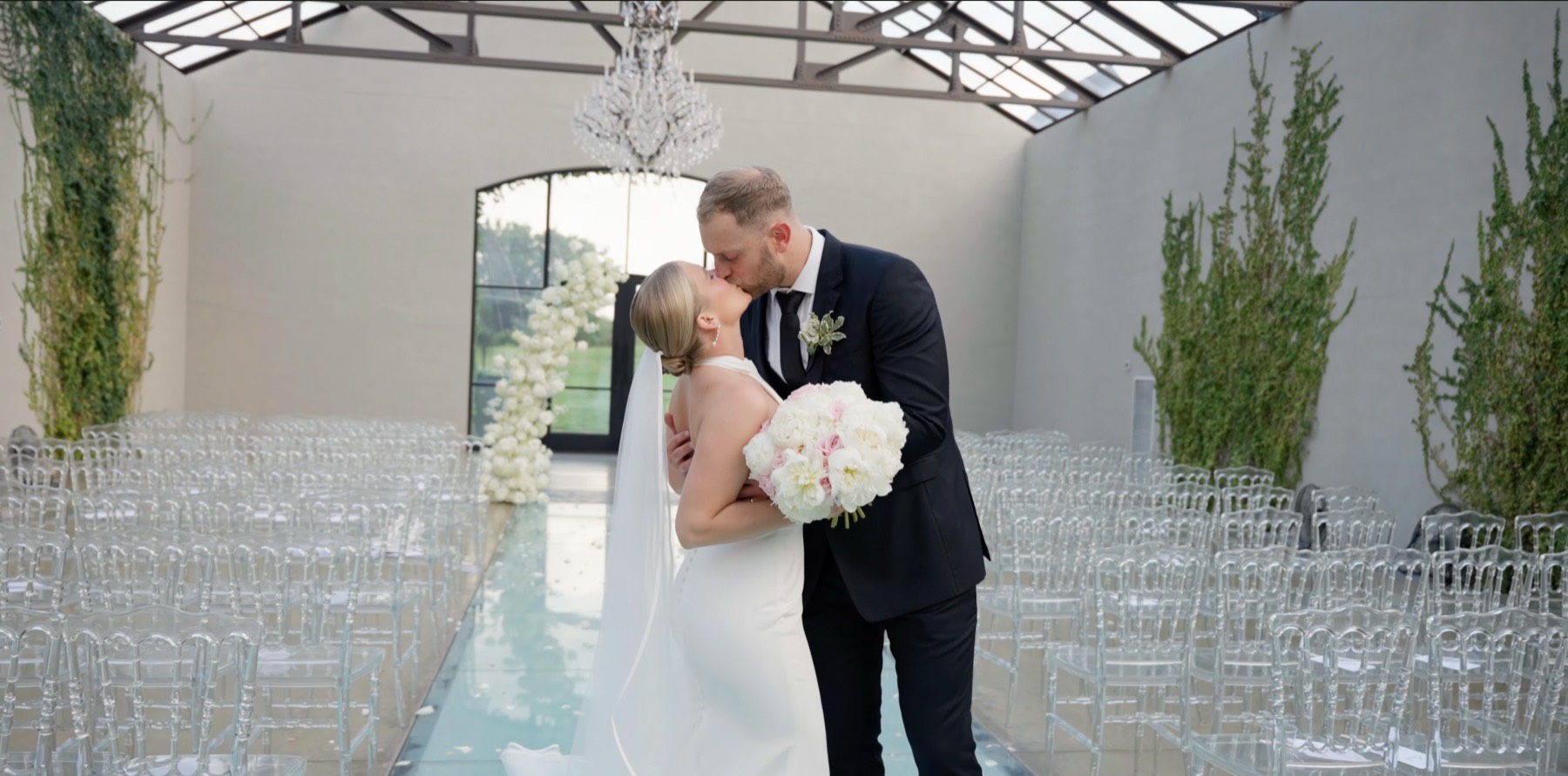 The first kiss at the end of the aisle, beneath a chandelier and a glass roof